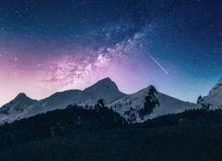 Night sky with a shooting star above mountains.