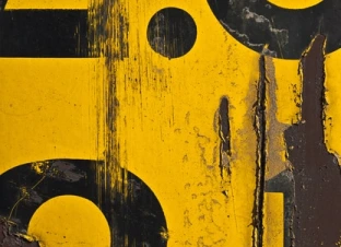 Close-up of a weathered yellow and black sign.